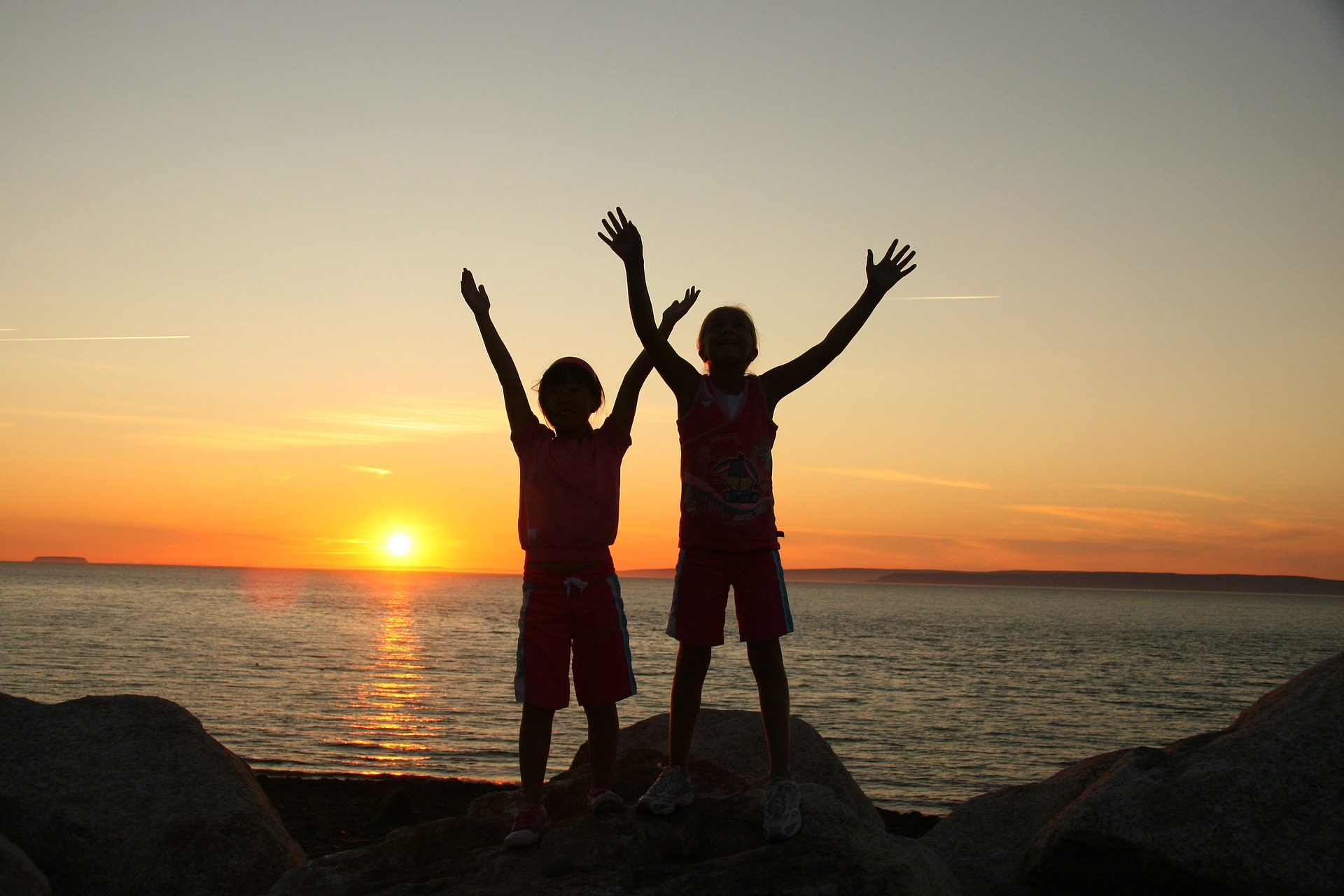 Children with arms raised at sunset by the ocean, expressing joy, freedom, and praise to God