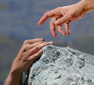 A hand reaching down to help another person climbing a rock, symbolising God helping believers when faith feels weak