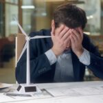 Stressed man at office desk holding his head in his hands, symbolising worry and the need to cast cares on God.