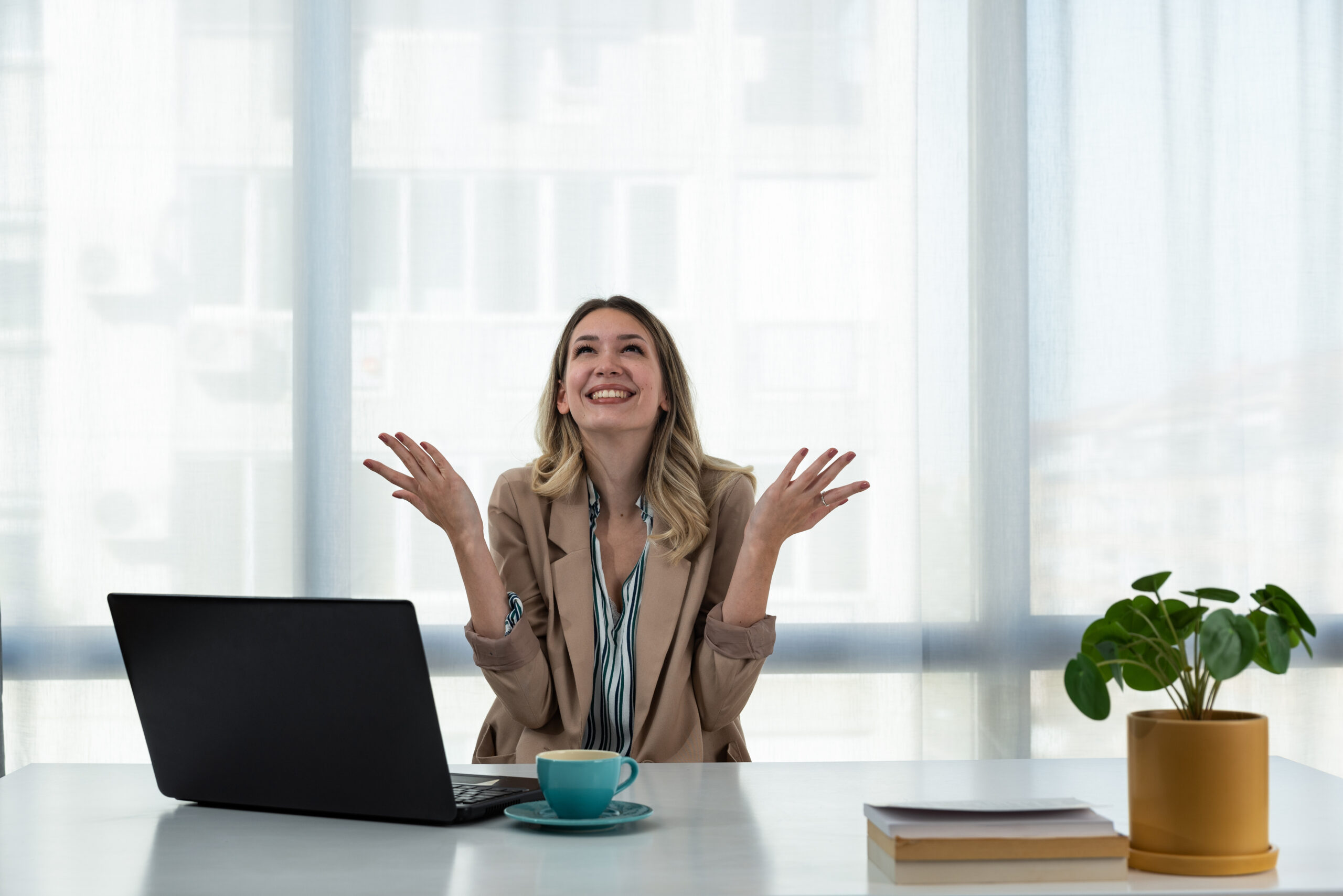 Woman in a modern office looking upward with open hands, reflecting trust, faith, and clarity in business decisions